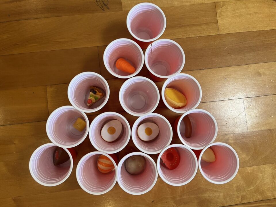 カップに食べ物のおもちゃを一つずつ入れています